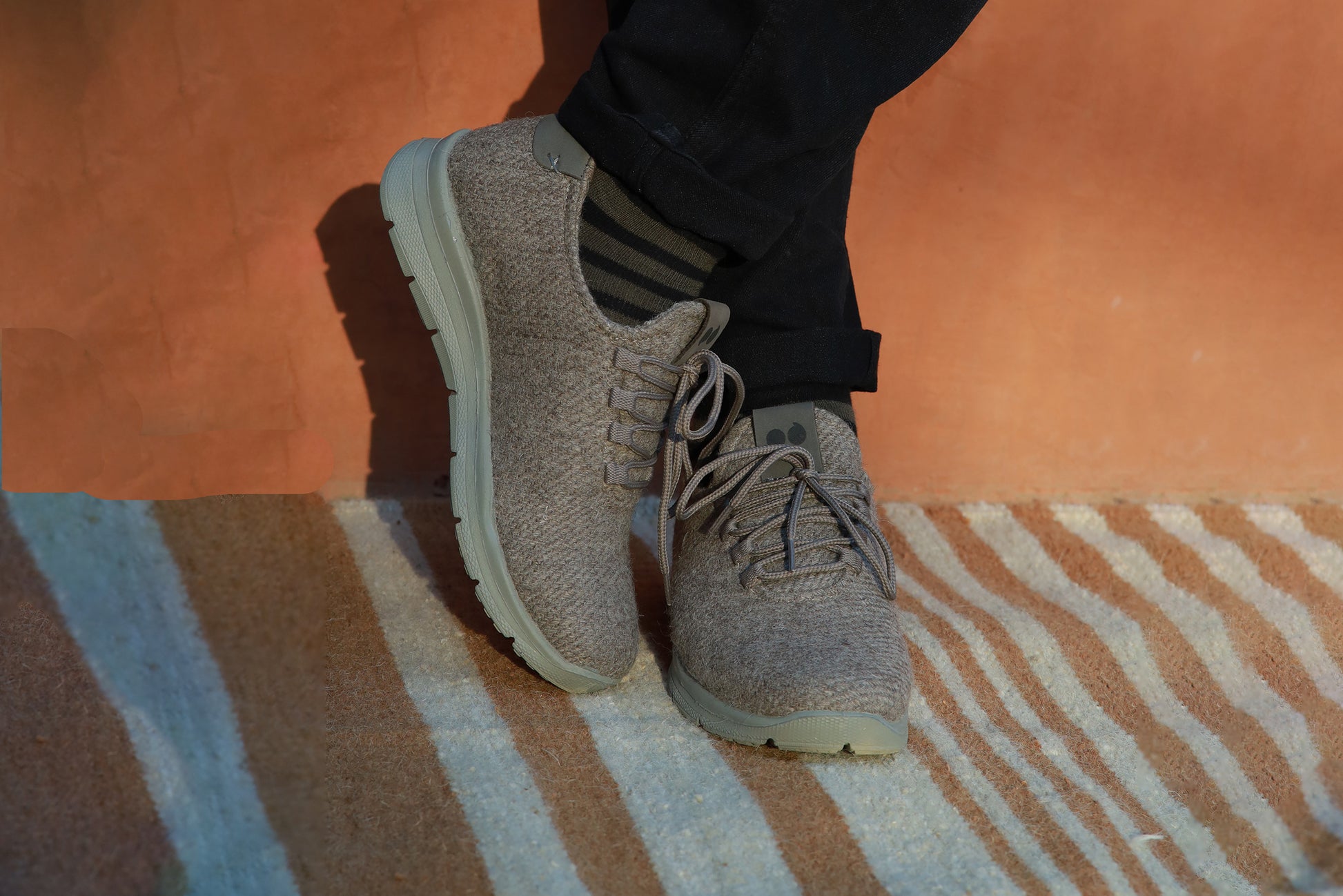 Person wearing stylish grey casual shoes with dark jeans on a striped rug.